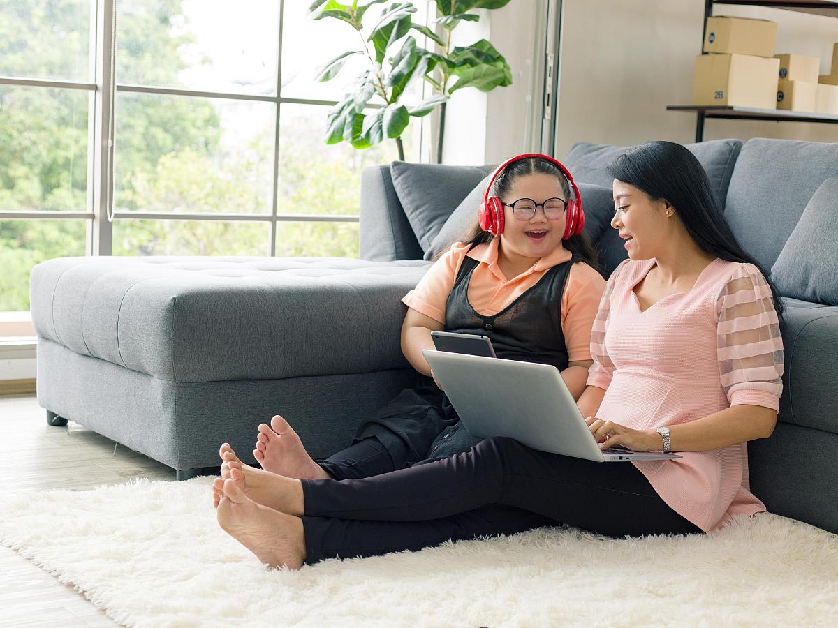 Autistic teenage girl playing on tablet sitting next to mom with laptop