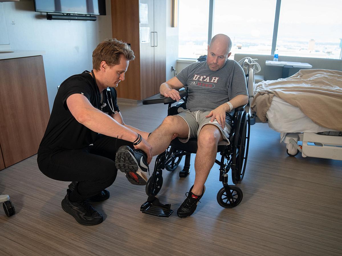 A U of U Health team member checks on a patient in a wheelchair during rounds.