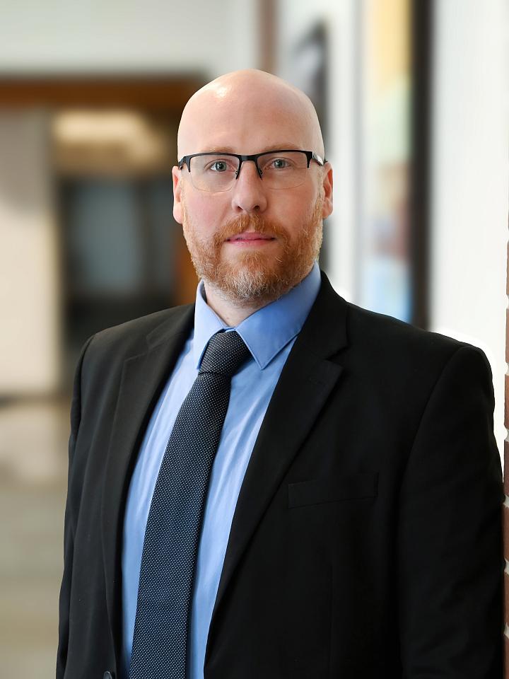 Professional headshot of a light-skinned bald man with a short red beard and glasses