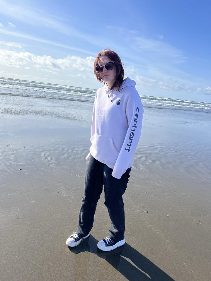 Sammy, a Teenscope program participant, stands on the beach in the sun with a hoodie and and black pants