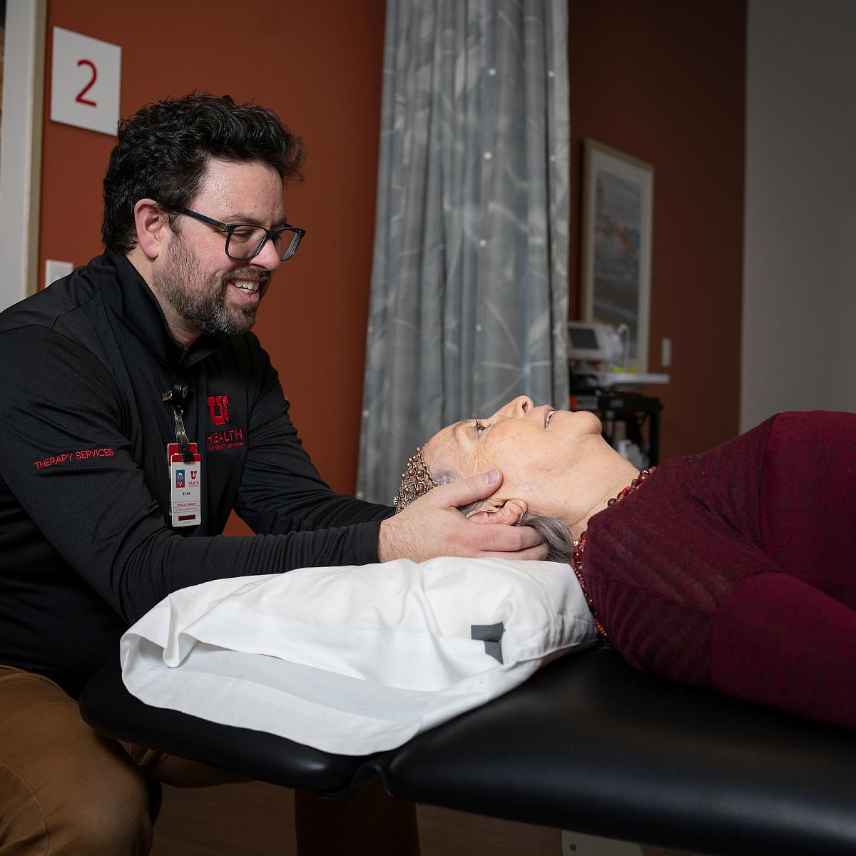 A male U of U Health physical therapist gives a female patient a neck massage