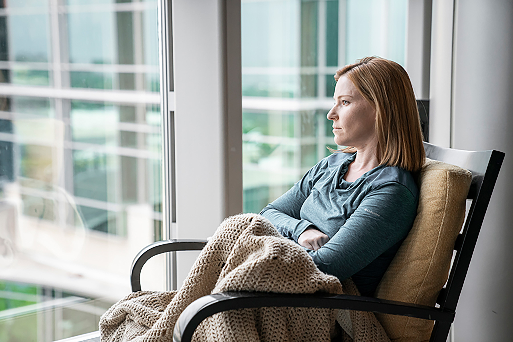 Woman sitting in chair with a blanket on her lap while staring out a window