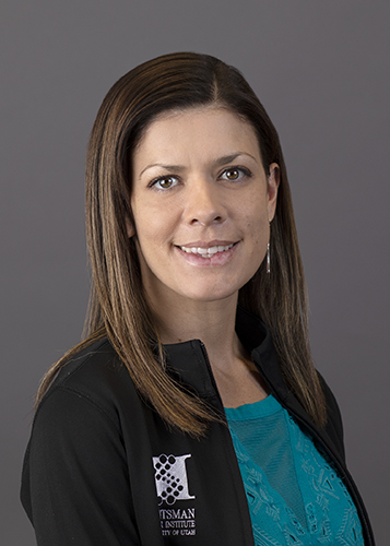 Melanie Ward wearing blue top with black jacket in front of grey background