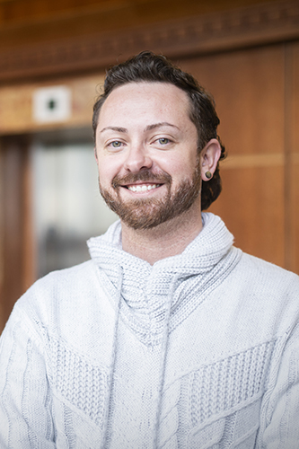 Shawn Newton smiling wearing a white patterned sweater in front of elevators