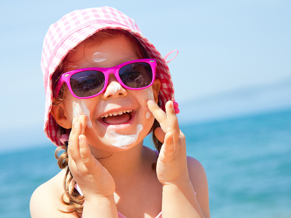 Girl happily applies sunscreen to face while at the beach