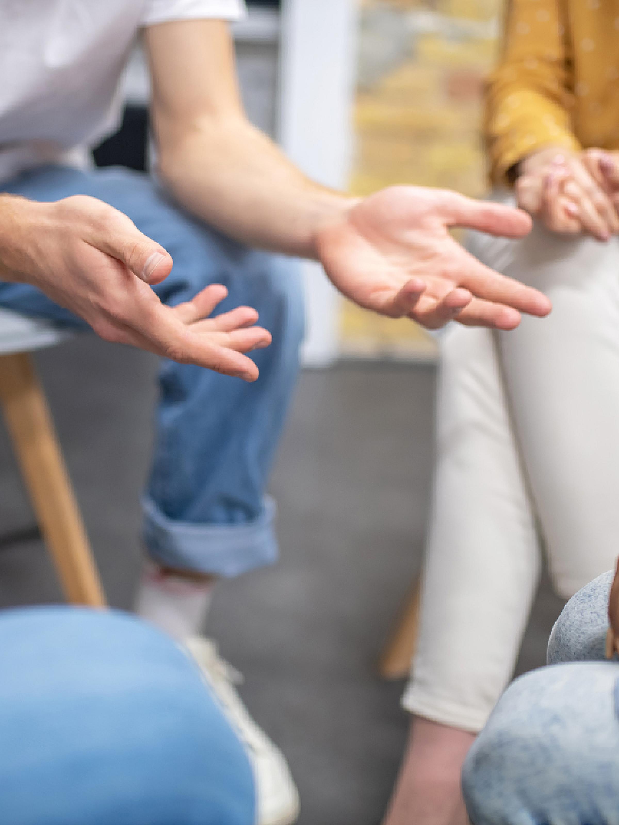 Close up of a group of people sitting in a circle, gesturing with their hands