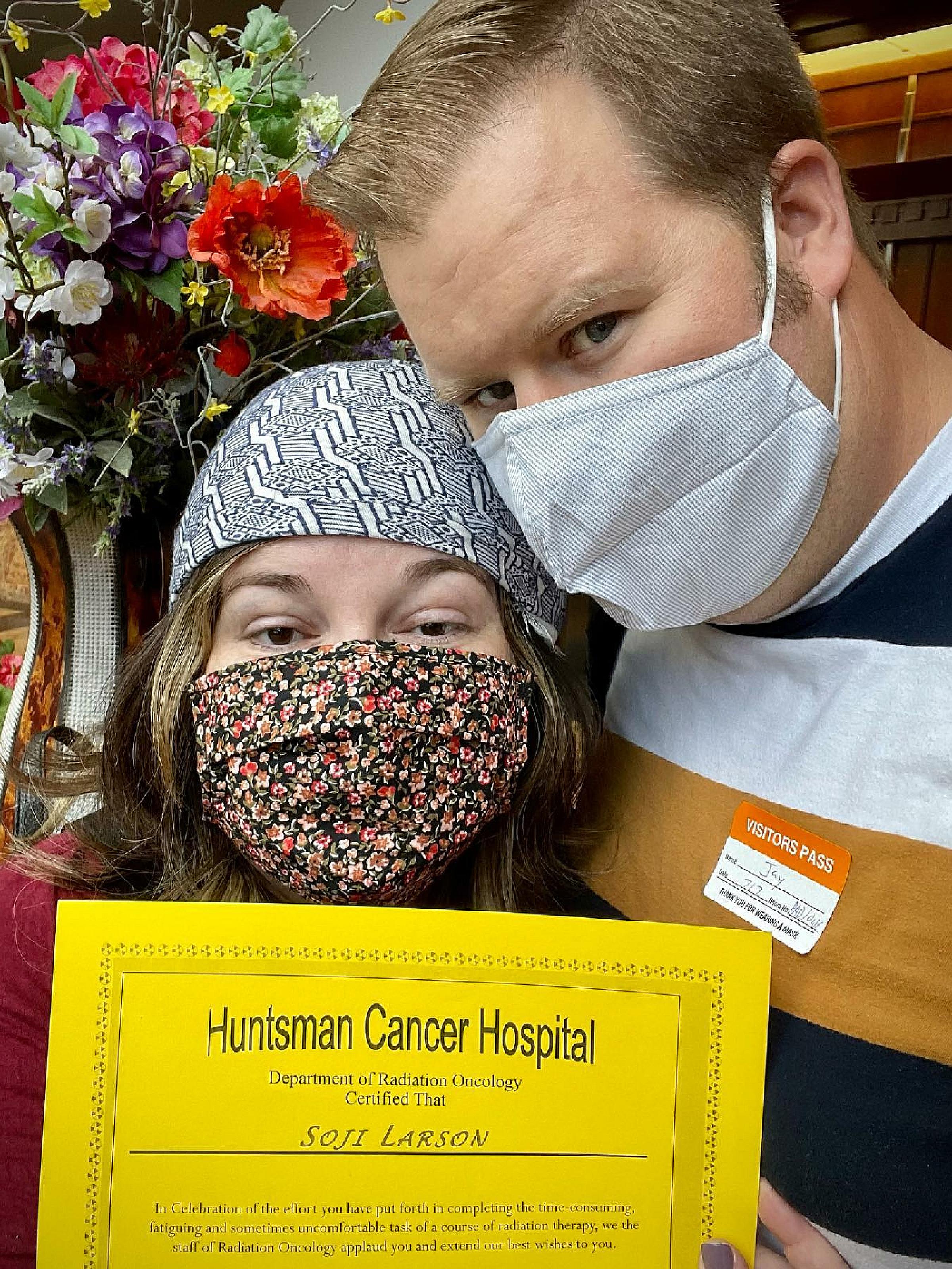 Jay and Soji Larson wear masks in Huntsman Cancer Institute while Soji holds up a certificate of completion for her radiation therapy treatment