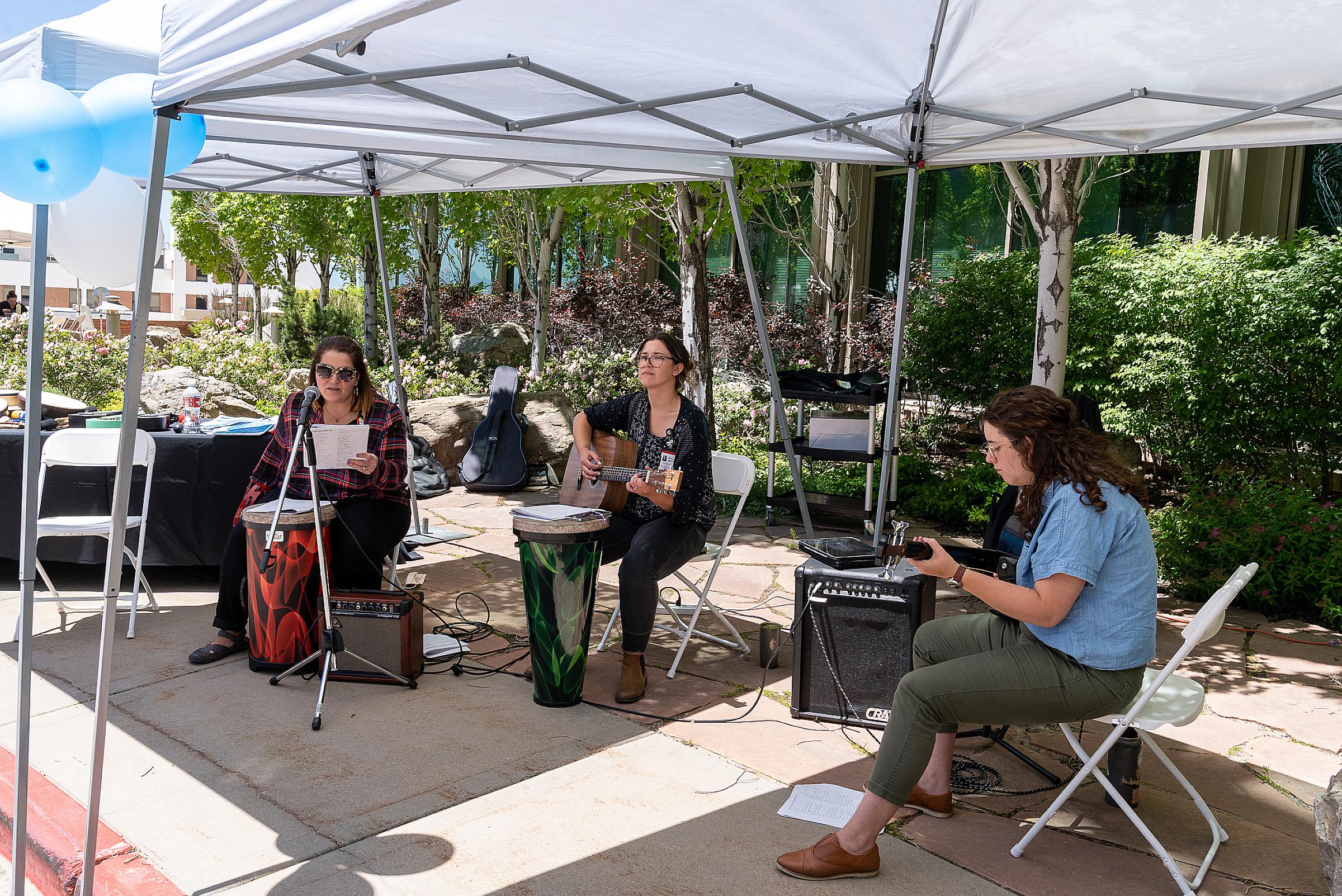 Three music therapists playing guitars and a drum outdoors at Huntsman Cancer Institute