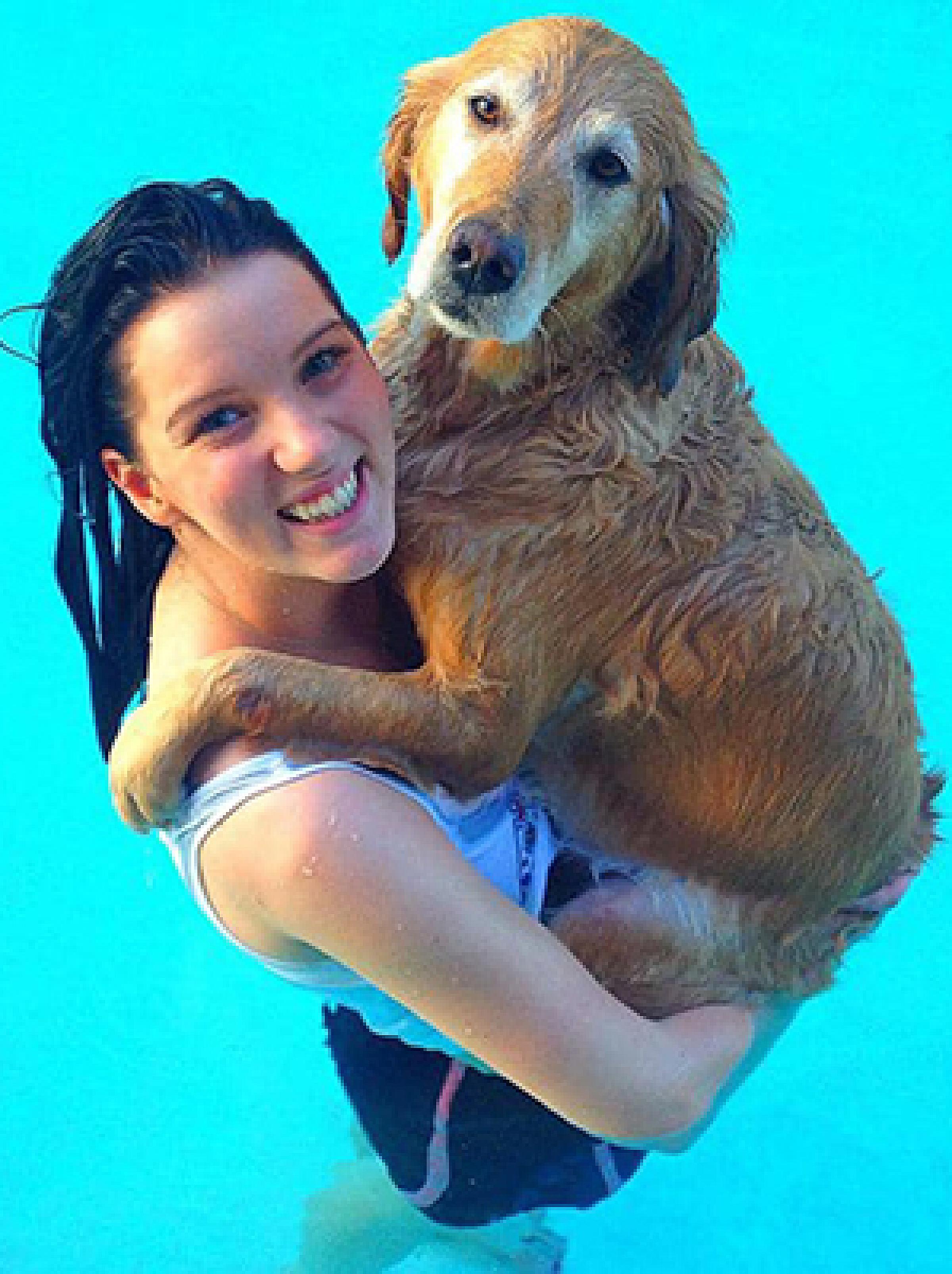 Natalie in a swimming pool holding a golden retriever and smiling