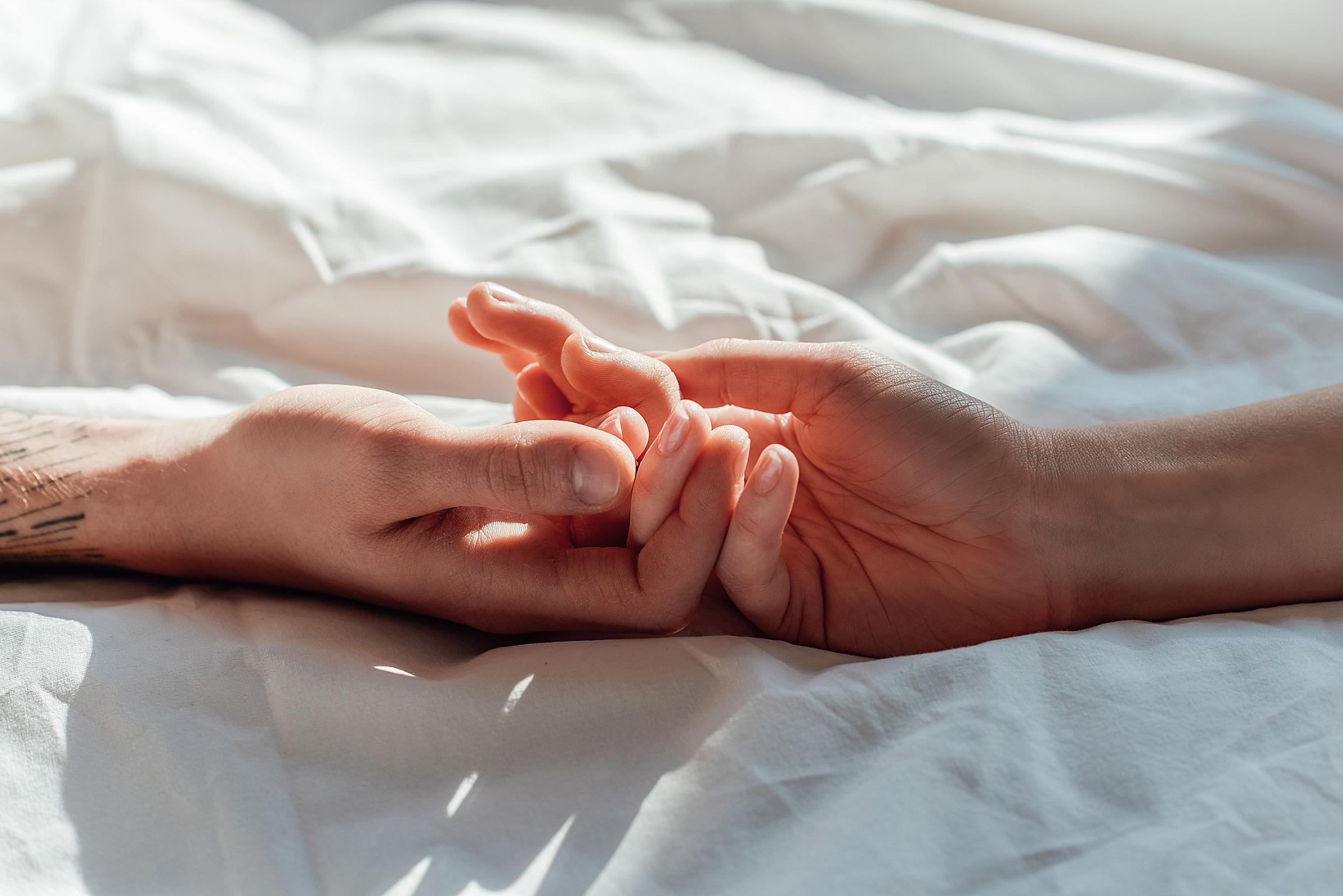 Close up of two hands, fingers interlaced on top of a bed