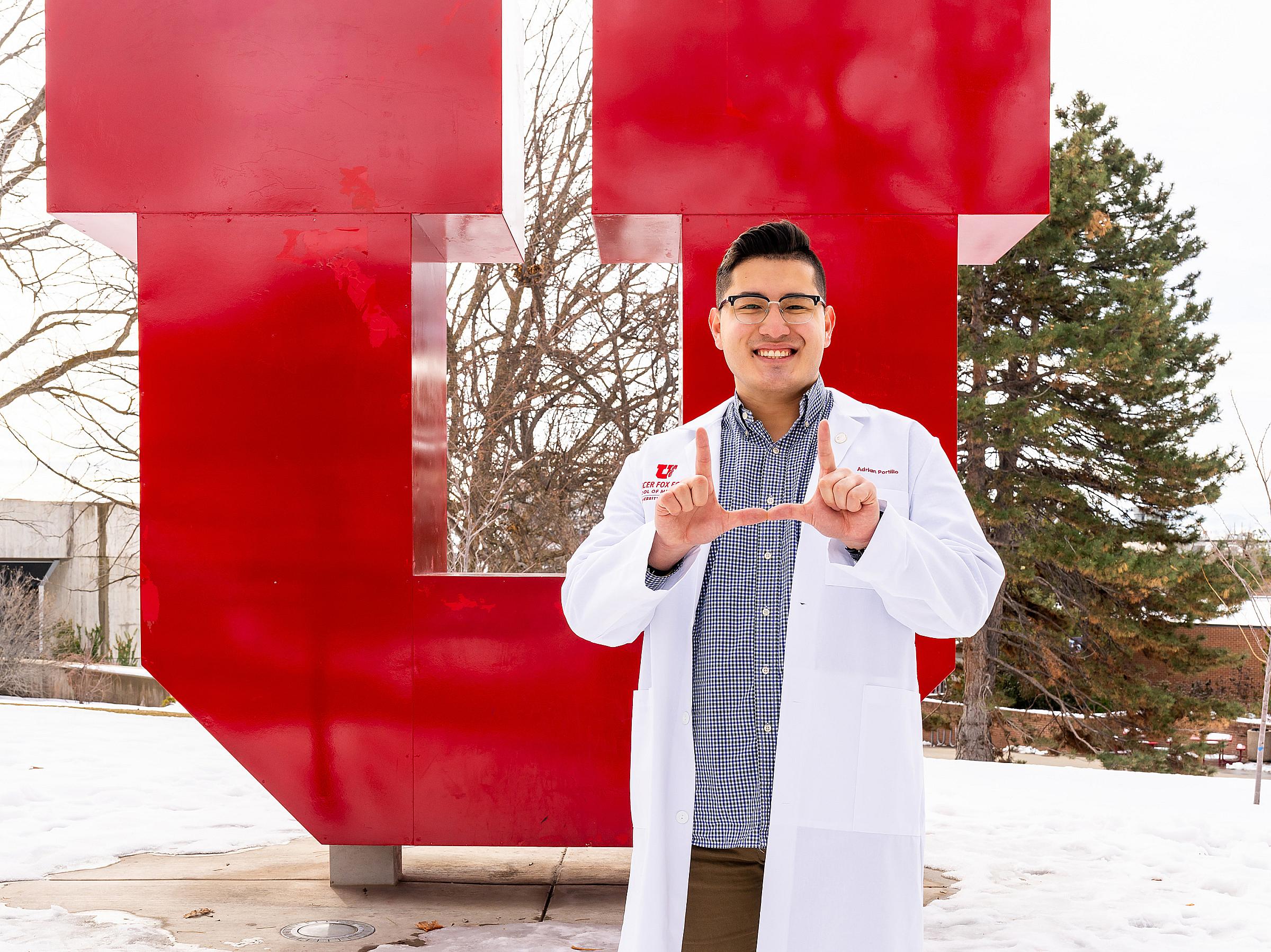 Adrian Portillo holding his fingers in a U shape while standing in front of a large red U on the University of Utah campus