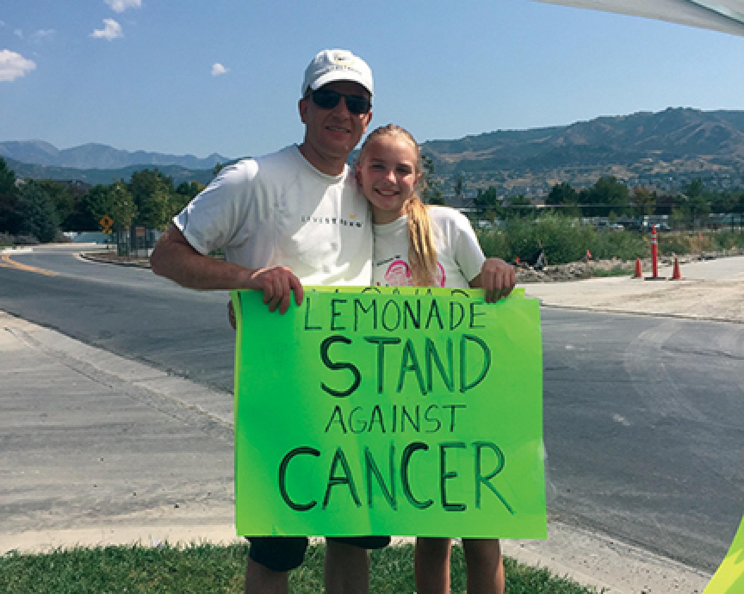 Adalyn Wood and her dad holding sign that reads lemonade stand against cancer