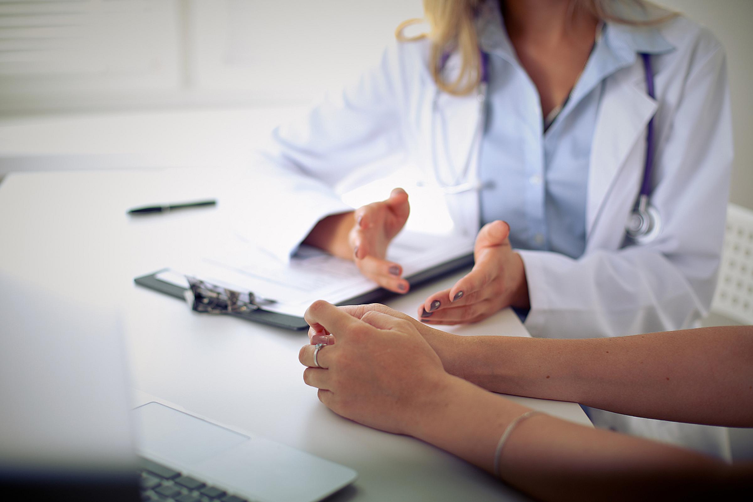 Close up on provider's hands gesturing over a clipboard while patient sits next to them