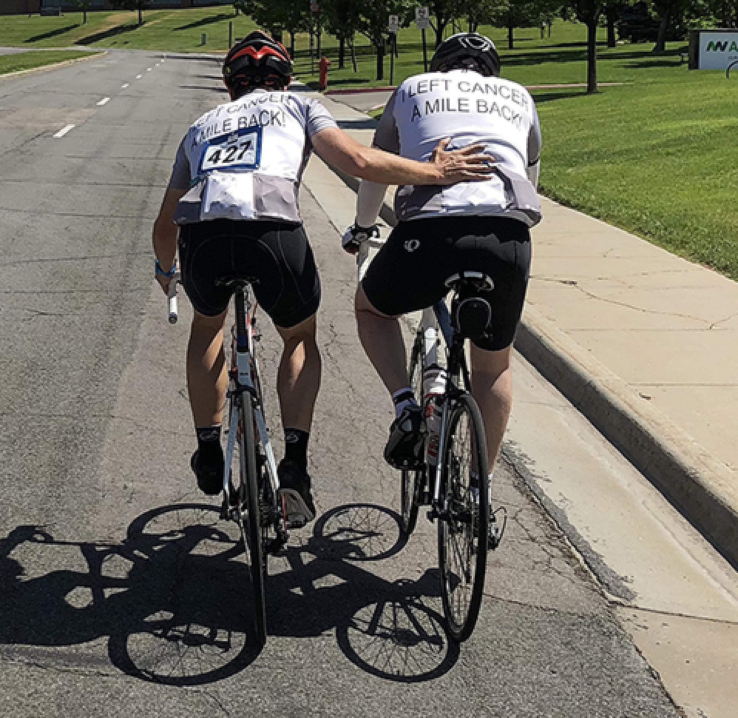 Dan Nelson and teammate road biking together with friend's hand on Dan's back