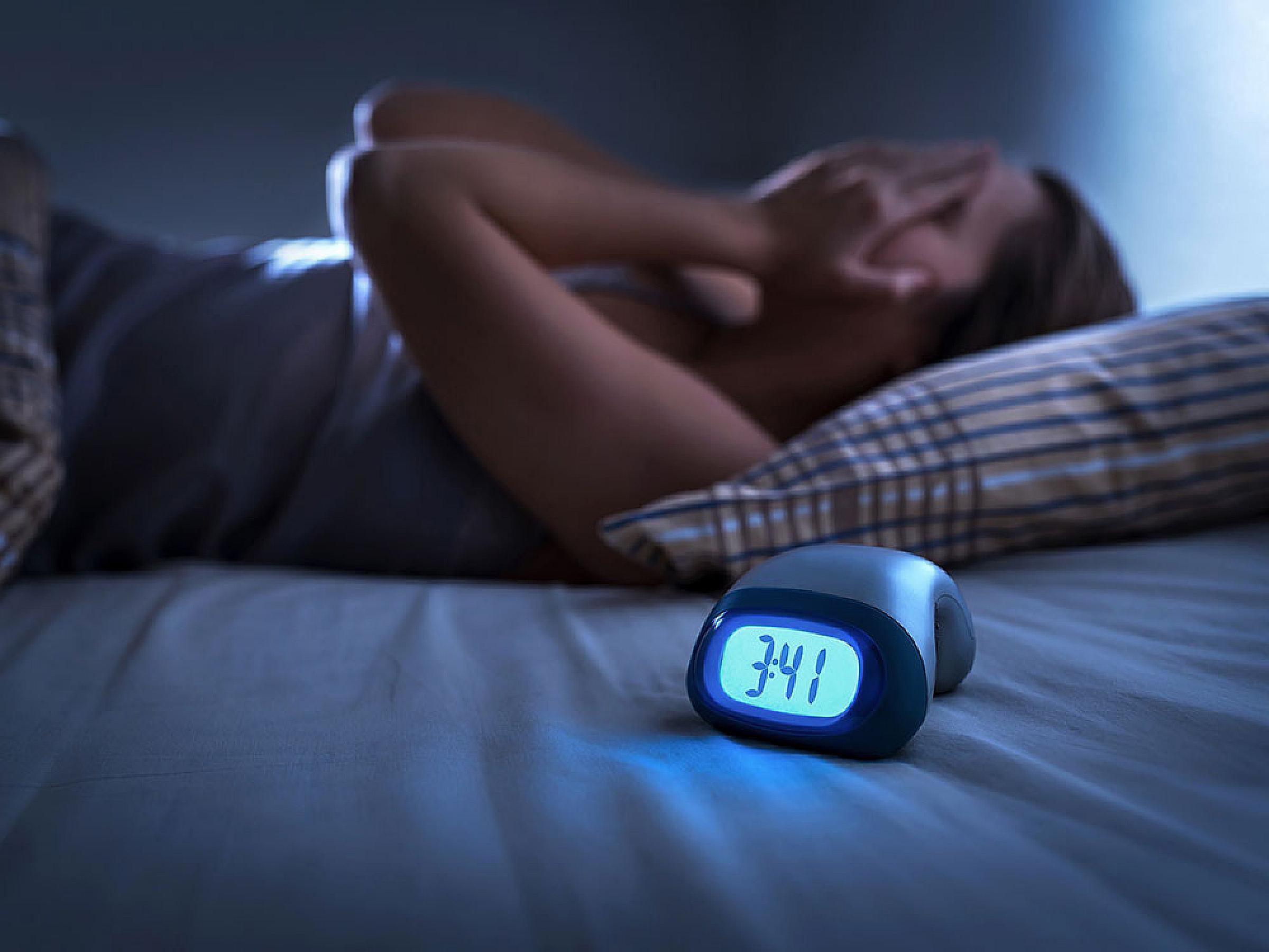 Woman lies in bed, covering face, while clock shows 3:41am
