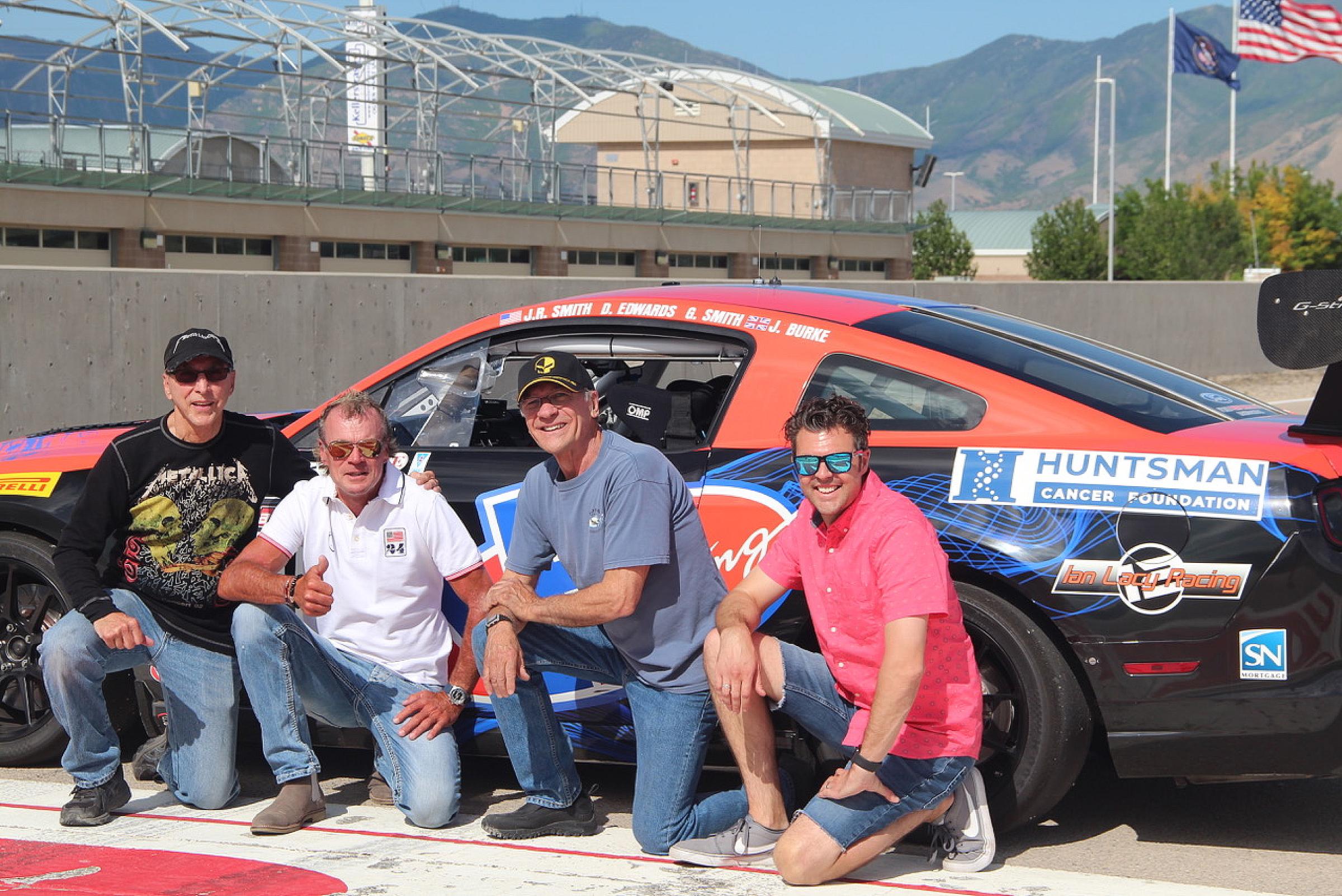 Four men kneeling next to a race car