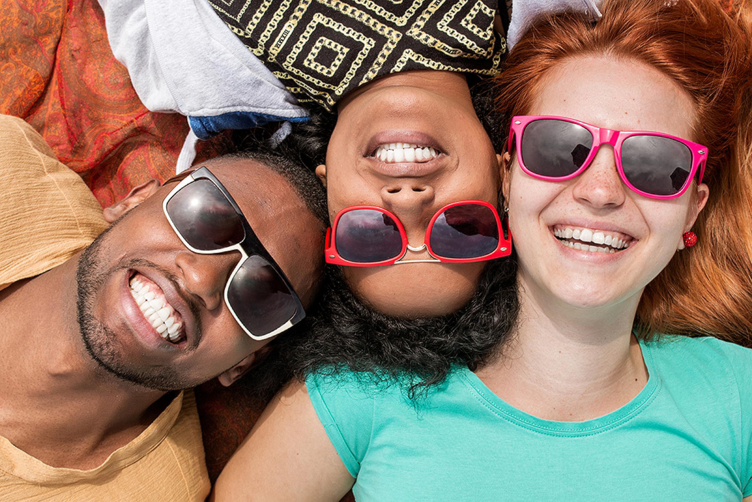 Three people lying on the ground and smiling while wearing sunglasses