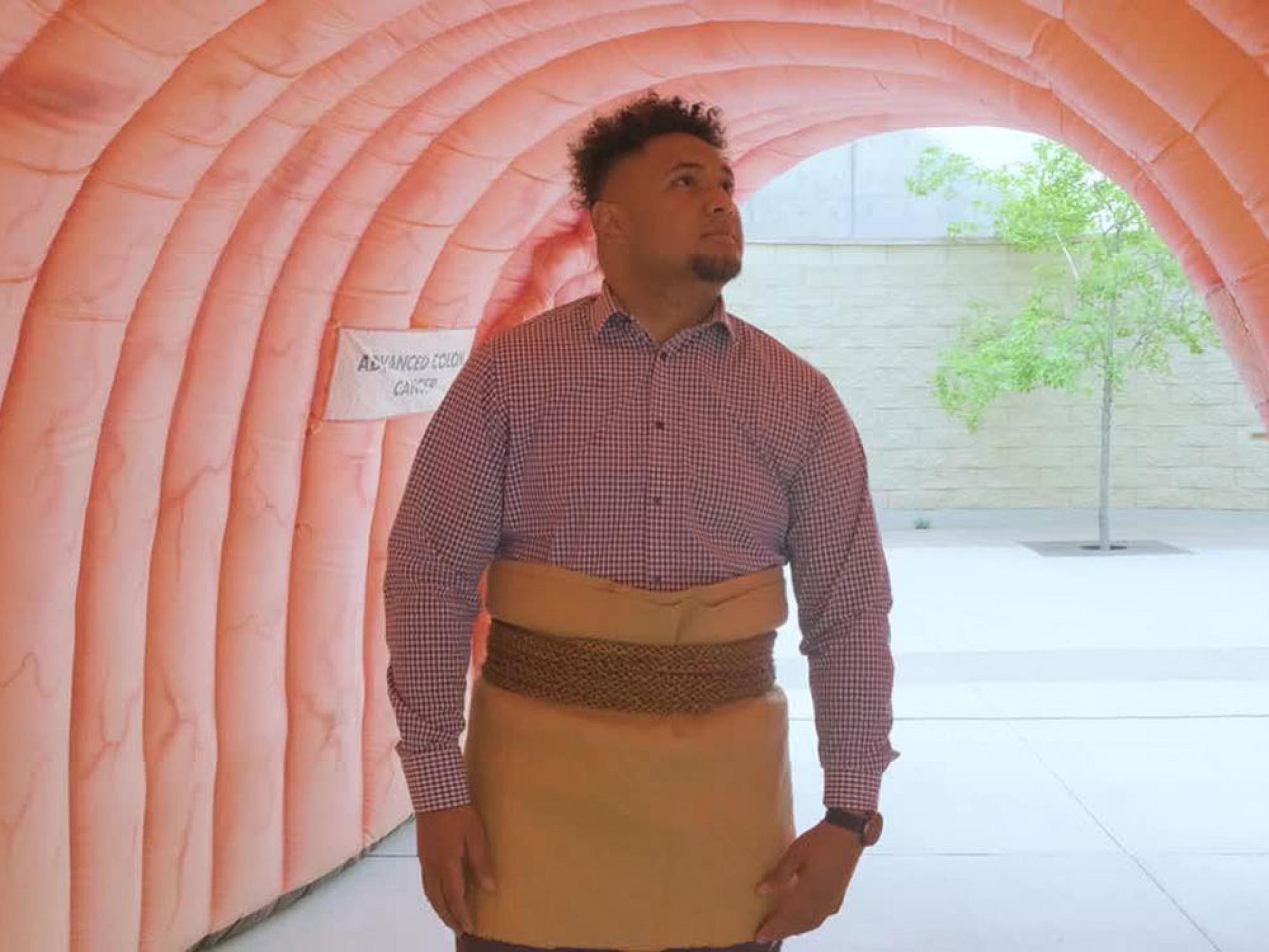 Will Satini wearing Maori skirt walking through colorectal exhibit