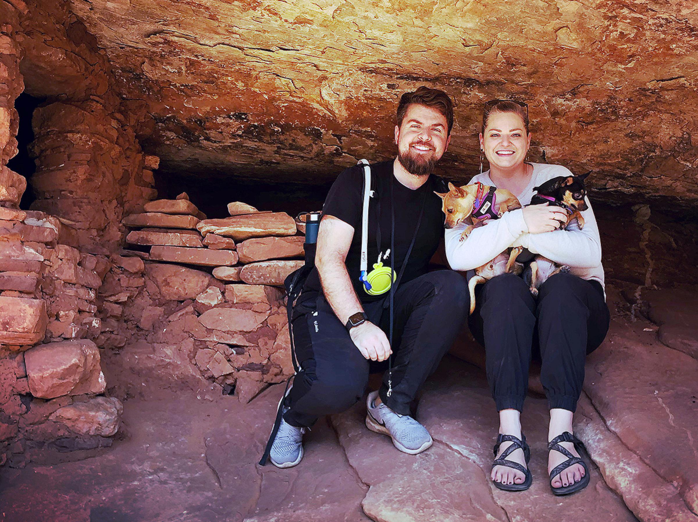 David and Shelli sitting near a structure in a cave and holding their dogs