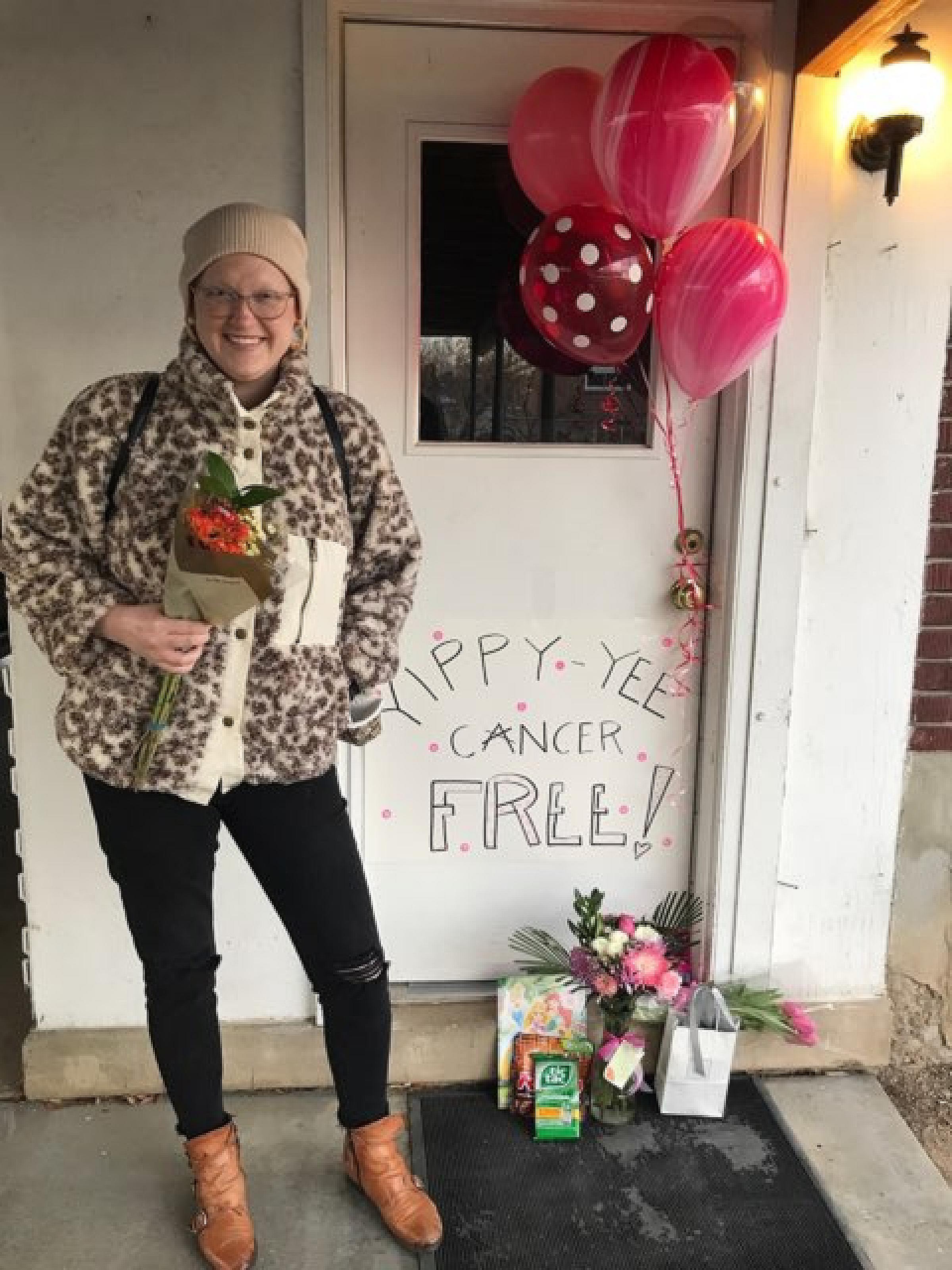 Laura Glissmeyer in front of presents, balloons, and a sign that says Yippy-Yee Cancer Free!