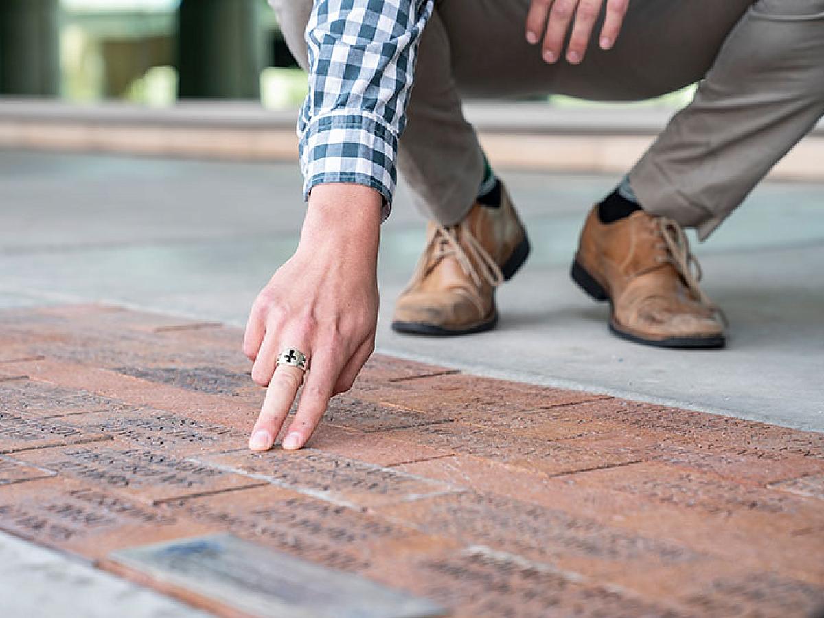 Man crouches to touch walkway paved with engraved bricks