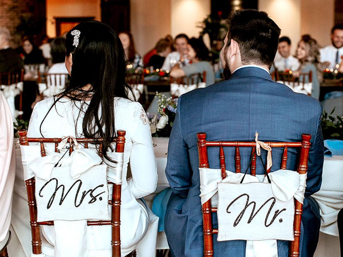 Bride and groom sit in chairs labeled Mr. and Mrs. at a wedding reception
