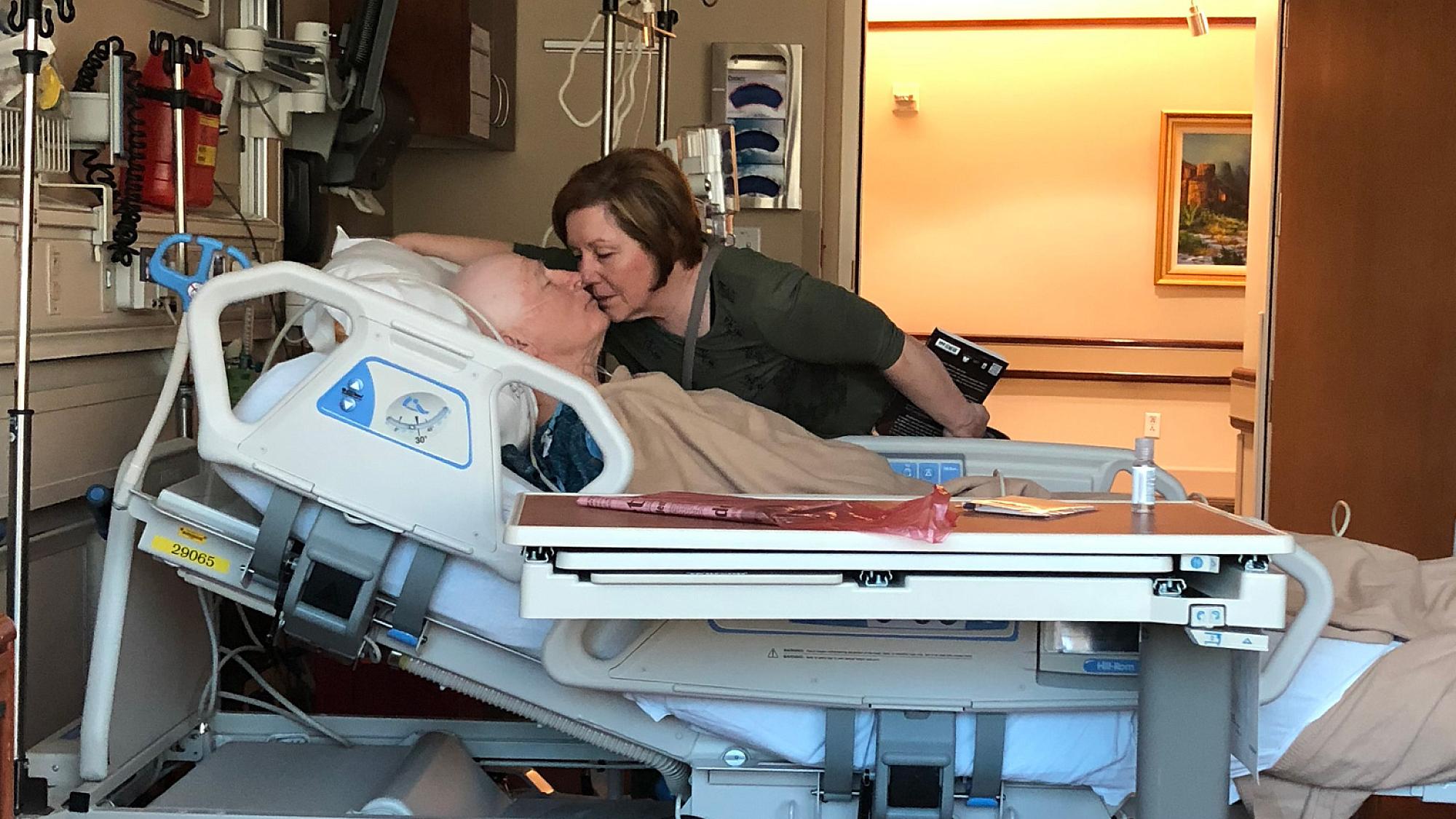 Jerry and Tad Simonson after his surgery in 2018. Jerry is lying in a hospital bed while Tad leans over to kiss him.