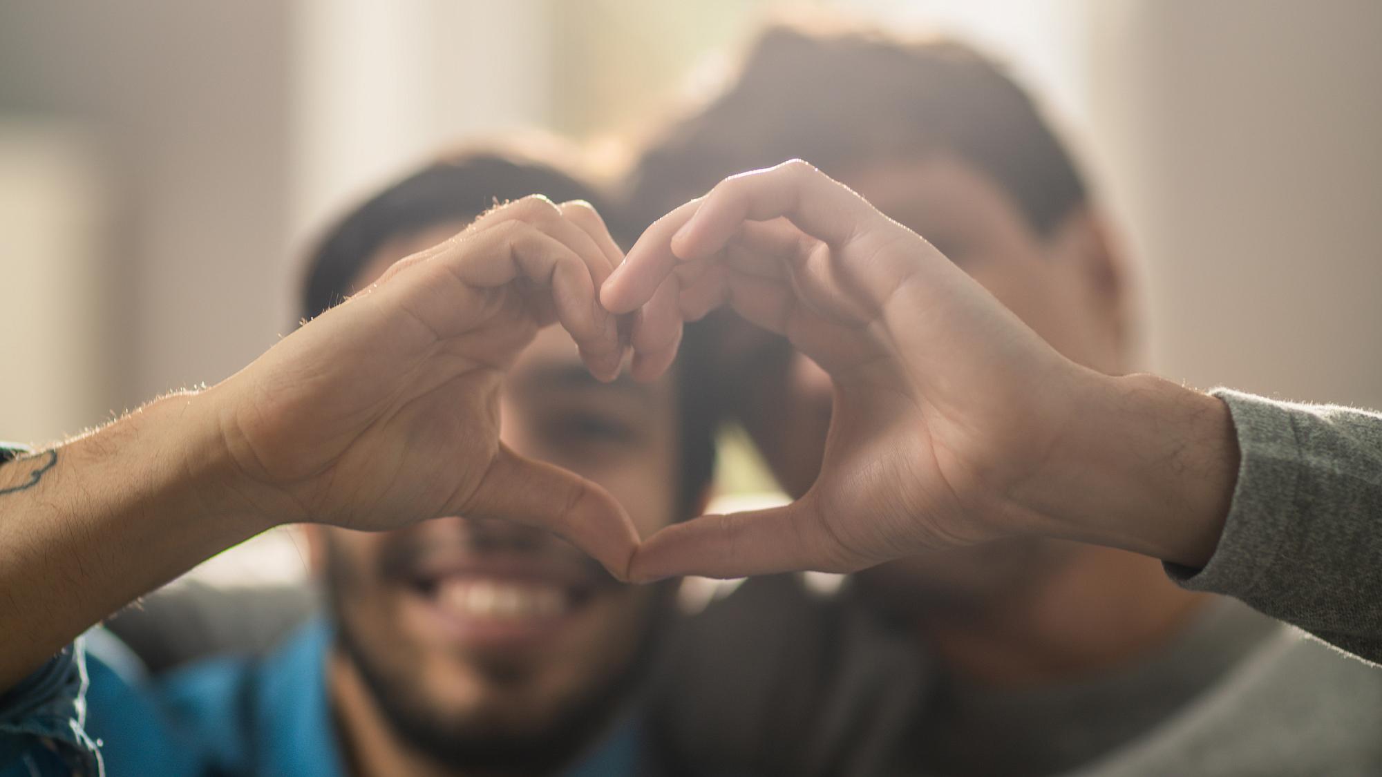 Blurry image of male couple holding their hands up to form a heart