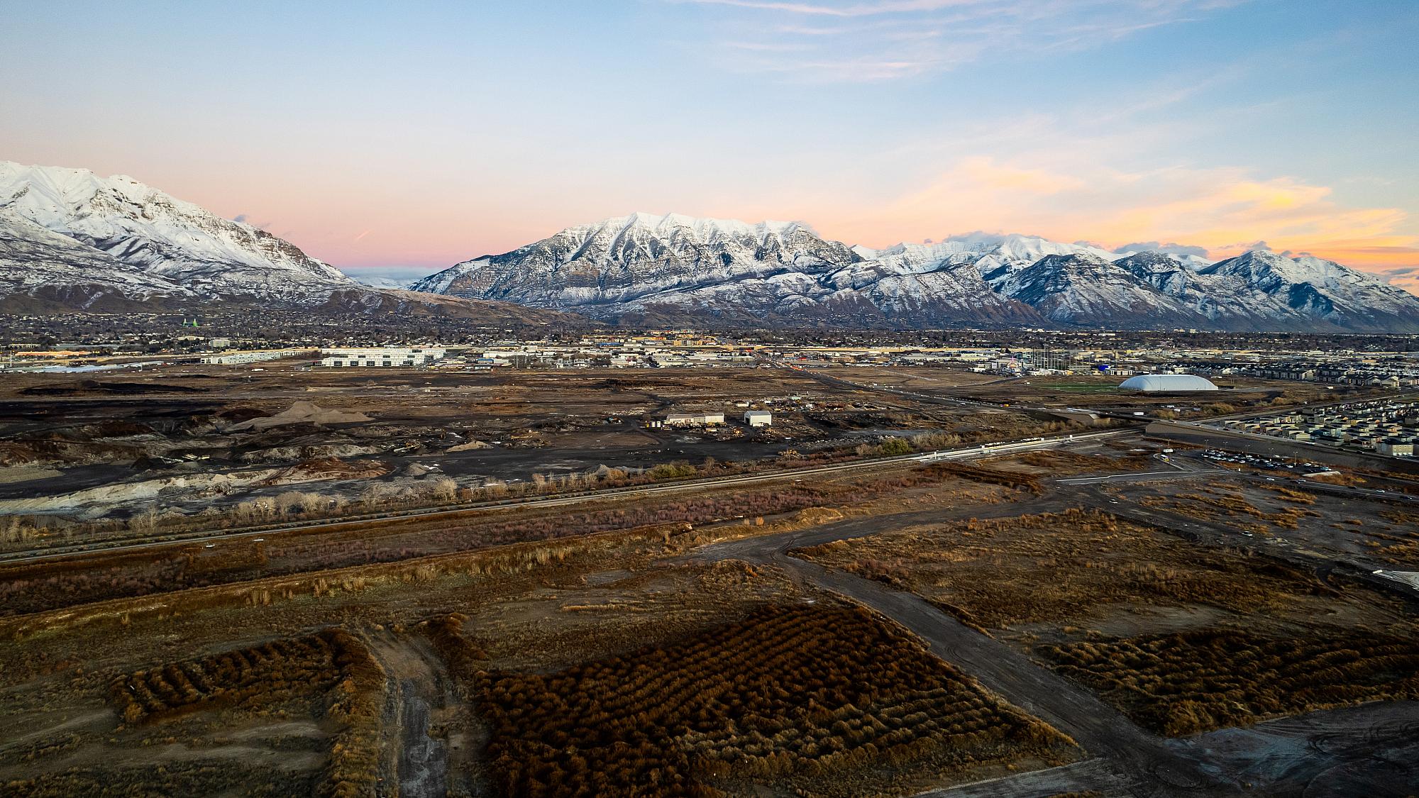 Aerial view of site where Huntsman Cancer Institute's Vineyard campus will be built; there are large empty fields stretching towards distant buildings and Mount Timpanogos in the background