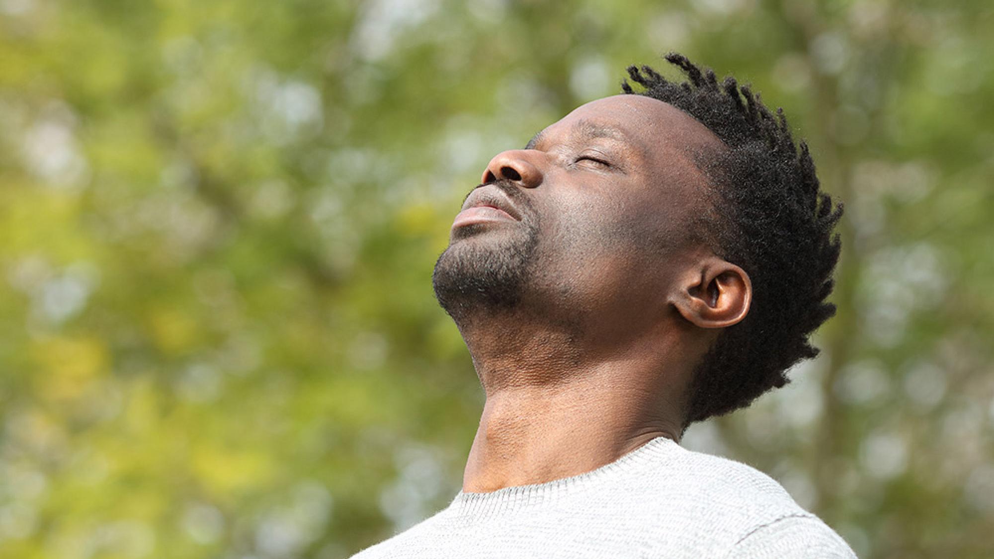Man standing outdoors and breathing in deeply with his eyes closed
