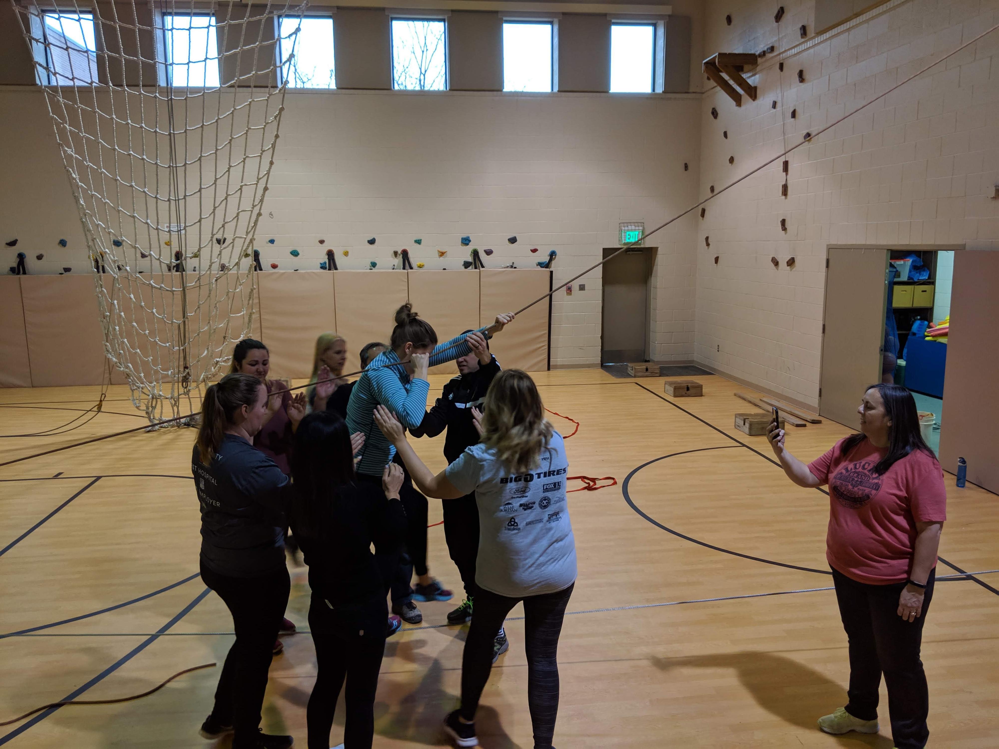 Group of people working as a team to climb through a low indoor ropes course challenge