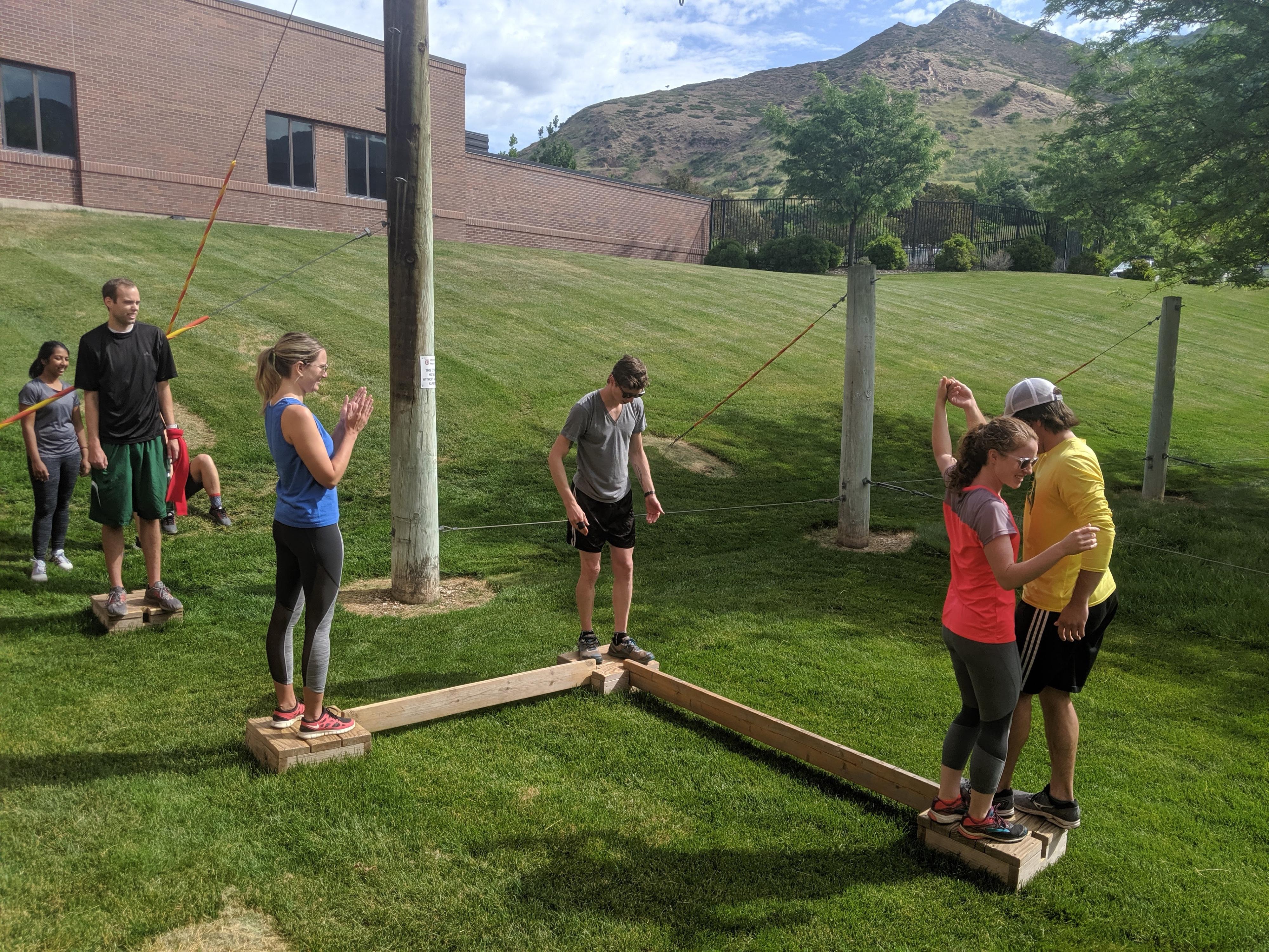 Group of people working as a team to climb through a low ropes course challenge