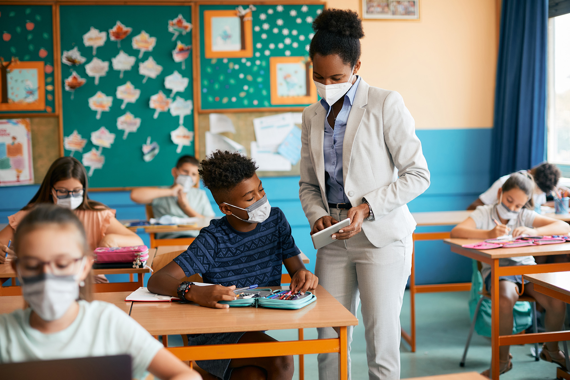 Teacher in classroom with children wearing masks.