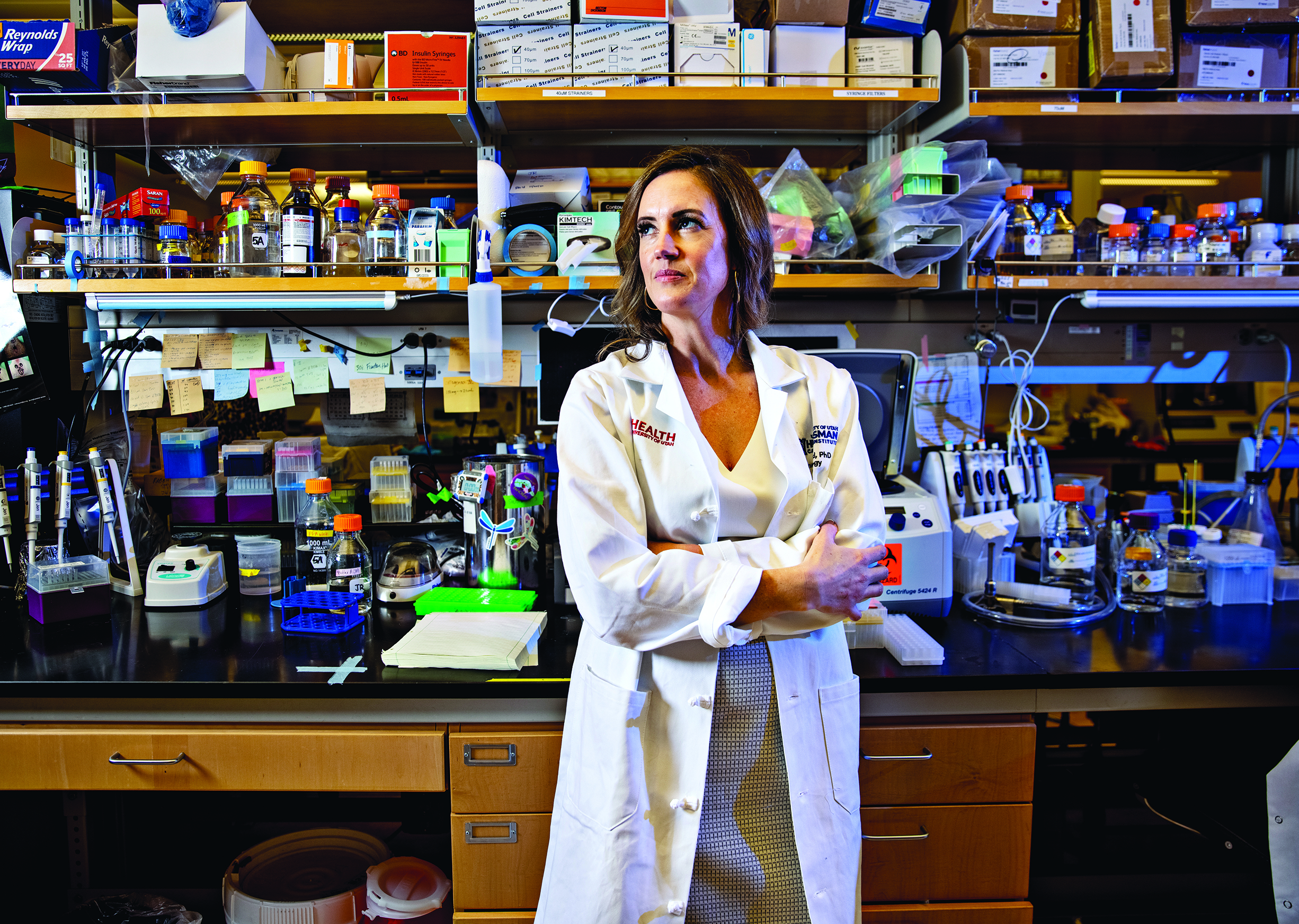 Professor June Round, PhD, standing in her laboratory. There is a lot of equipment on the shelves.