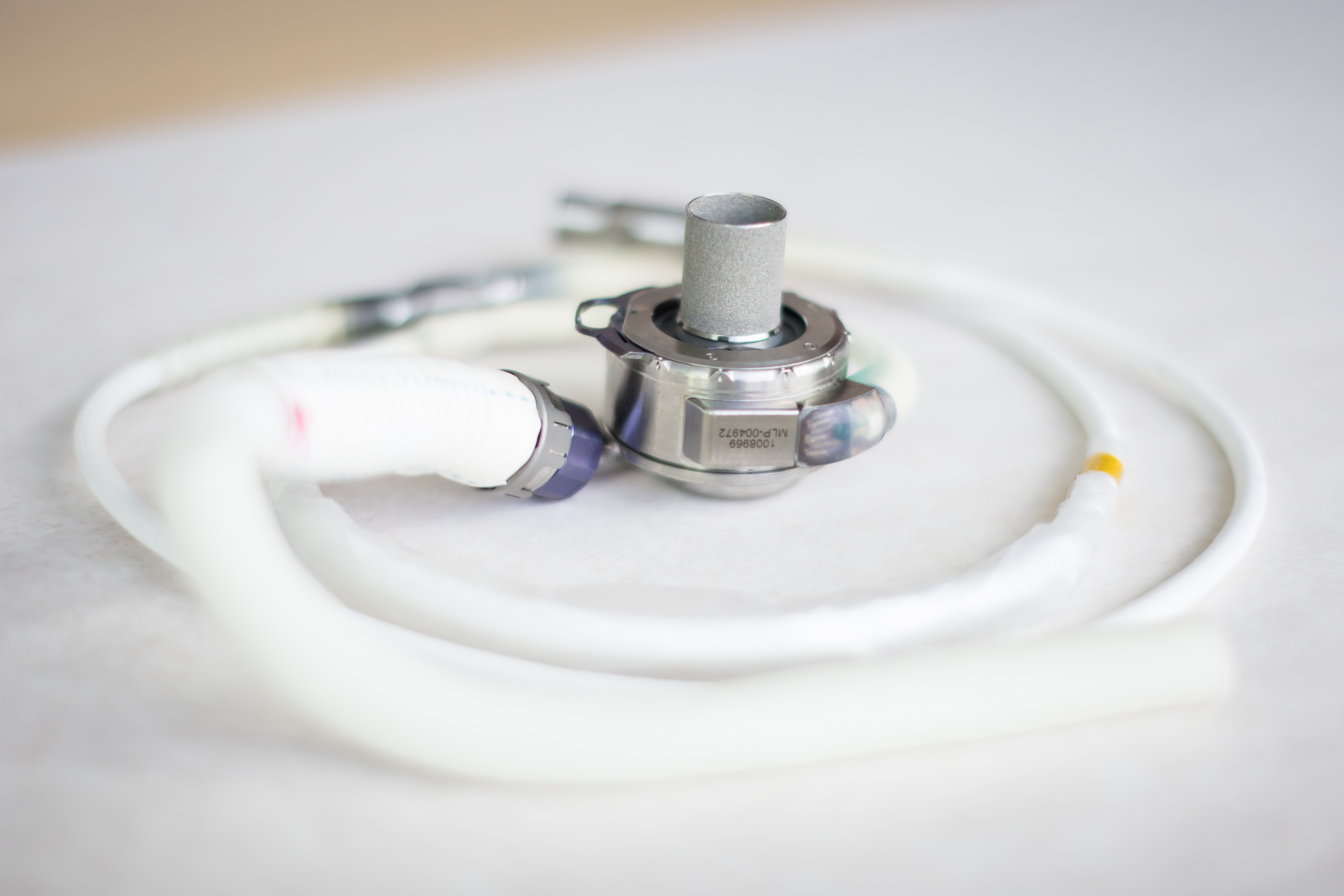 Close-up photo of a heart pump made of plastic tubing and metal, sitting on a white surface.