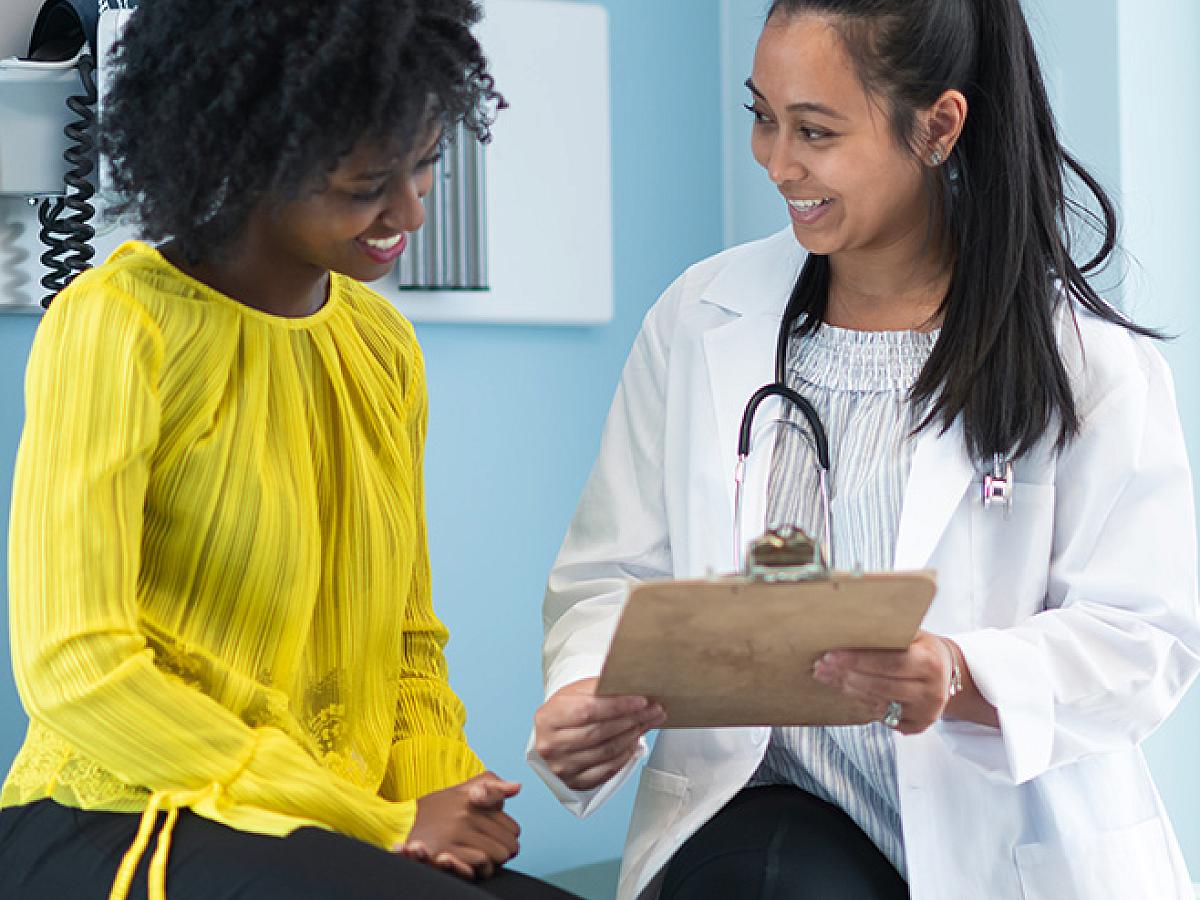 Black female patient smiling and talking with her female provider holding a clipboard