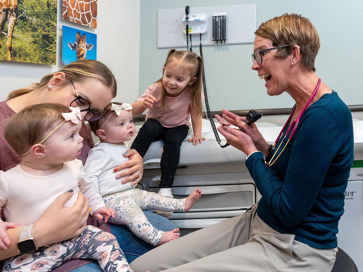 A mother with infant twin girls and a toddler talk to a U of U Health pediatrician