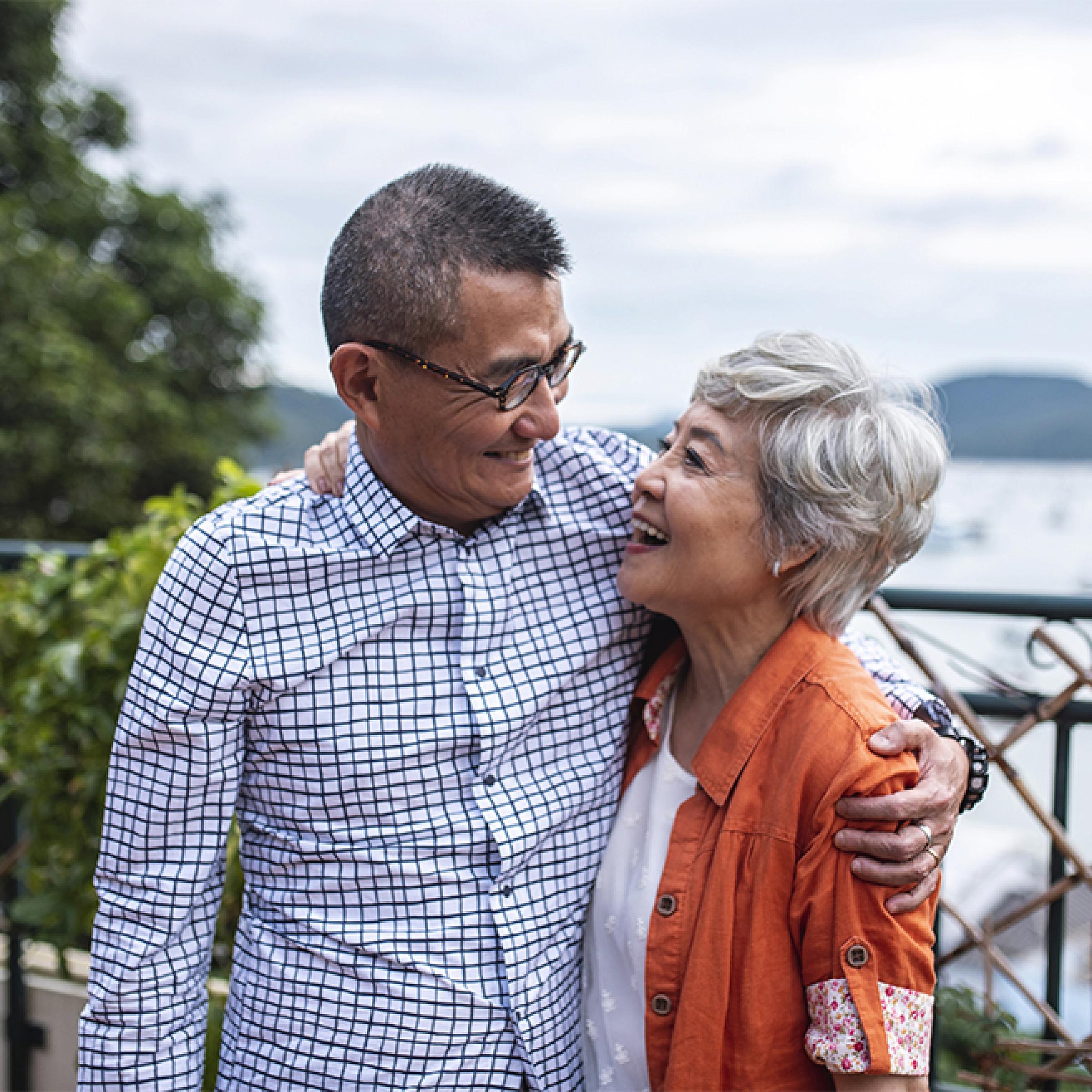 Smiling older couple looking at each other with arms around each other's shoulders