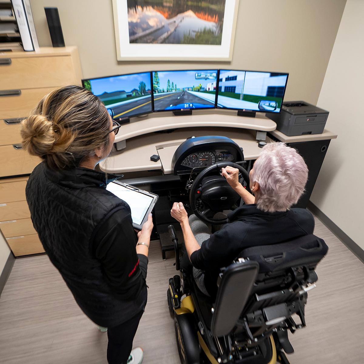 A U of U Health employee helps a woman use driving simulator at Sugar House Health Center