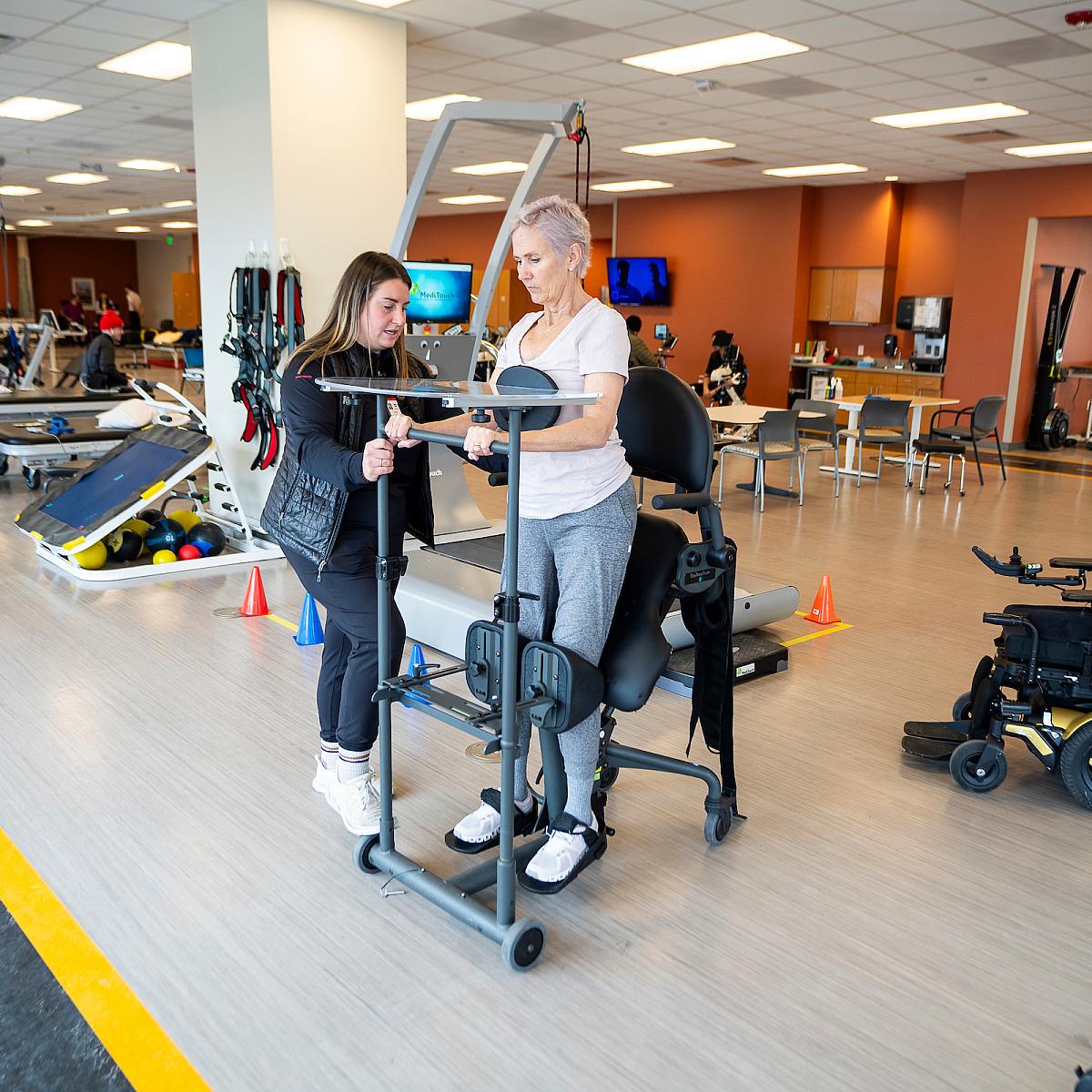 Female U of U Health employee helps a woman with a lift chair in a large gym