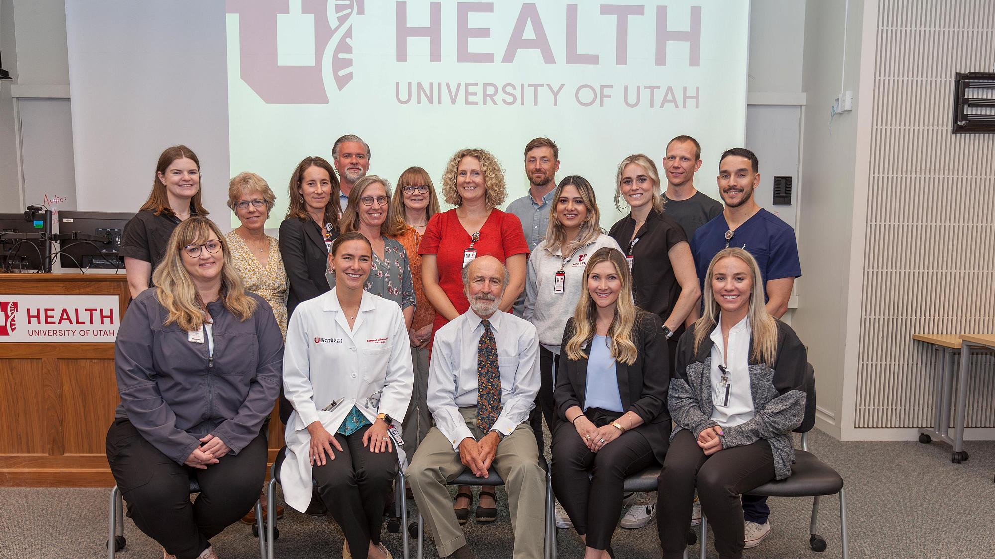 Group shot of ALS providers and staff sitting and standing in front of the U of U Health logo projected onto a screen
