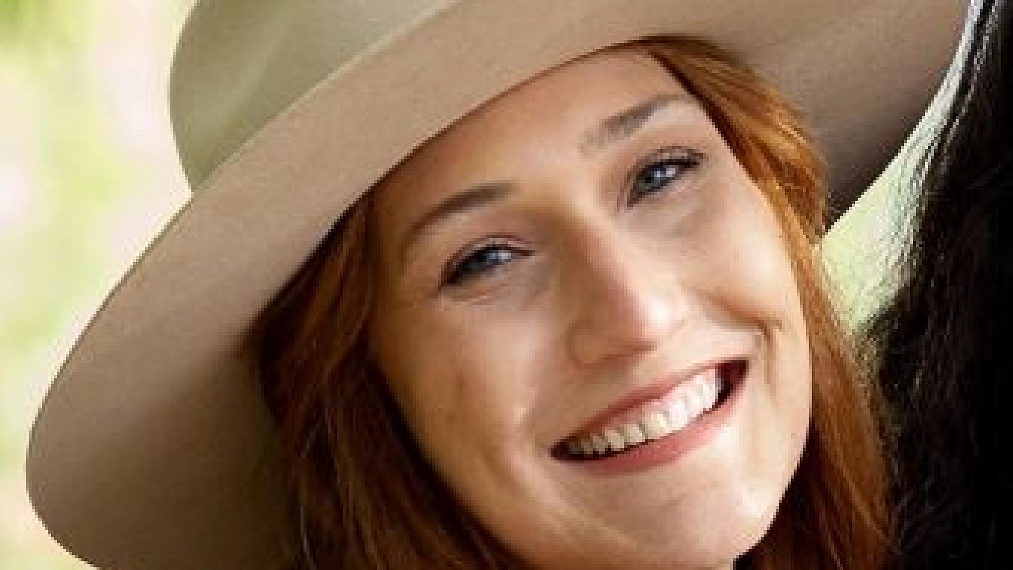 Alisa Hartline has long red hair and wears a beige hat outside.