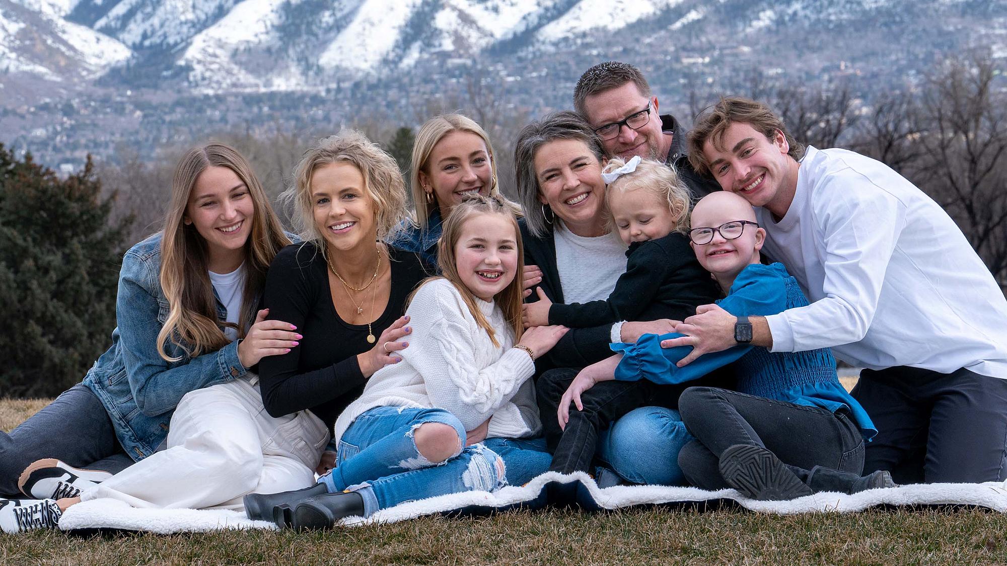 Stacie and her family of nine sit on a blanket outside and pose in a group hug